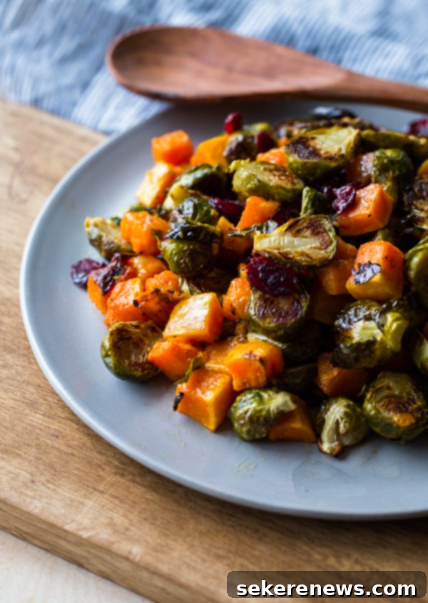 Roasted Brussels Sprouts and Squash with Dried Cranberries and Dijon Vinaigrette. This colorful Thanksgiving side dish recipe is easy and loved by all! #thanksgiving #vegetarian #sidedish #fall #holiday #recipe #abeautifulplate #squash #brusselssprouts Serving bowl of Roasted Brussels Sprouts and Squash with Dried Cranberries and Dijon Vinaigrette