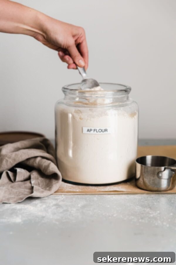 Mastering Flour Measurement 3 A person spooning fluffed flour into a dry measuring cup, ensuring it's not packed.