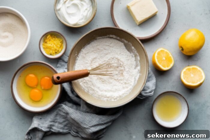 Zesty Lemon Pound Cake 4 A flat lay photograph showcasing all the room temperature ingredients needed for a delicious lemon loaf cake, including flour, sugar, butter, eggs, Greek yogurt, and fresh lemons.
