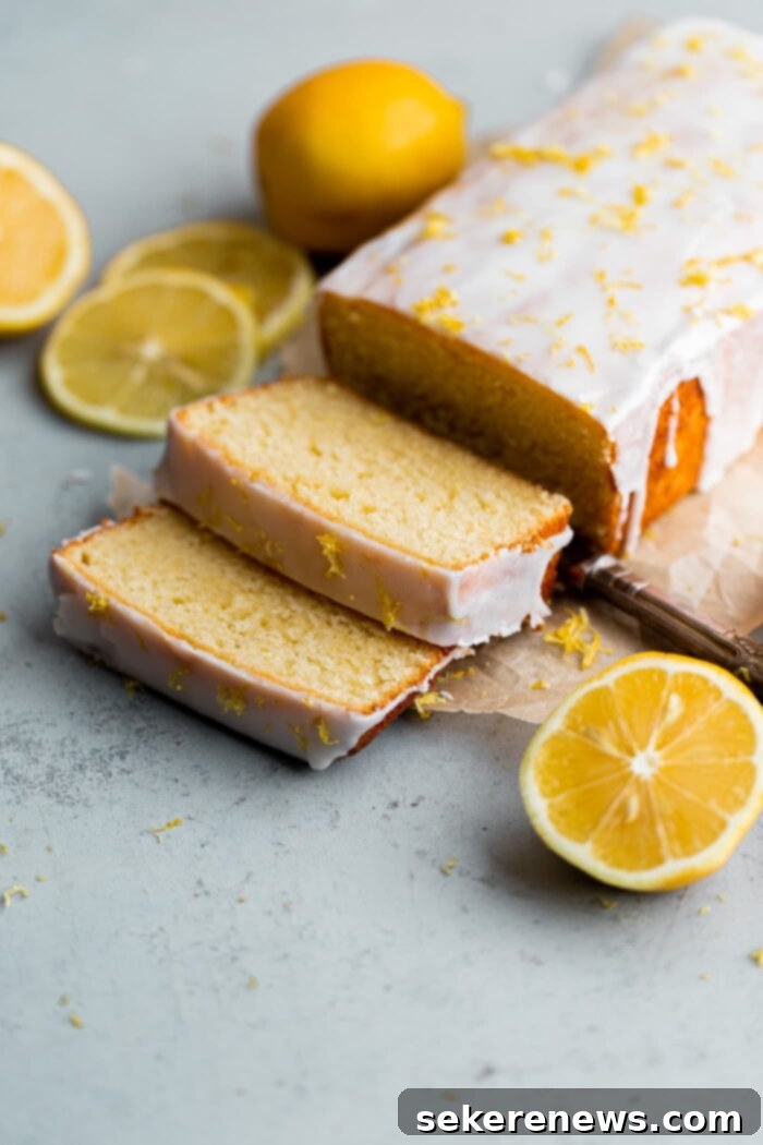 Zesty Lemon Pound Cake 7 A perfectly sliced lemon loaf cake displaying its moist, tender crumb and the thick, glistening lemon glaze on top, garnished with fresh lemon zest, on a rustic cutting board.